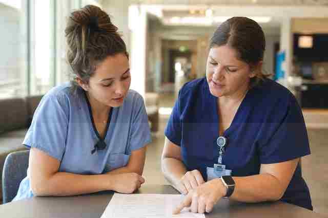 Surgical technology student in scrubs learning in an operating room with a clinical instructor beside them