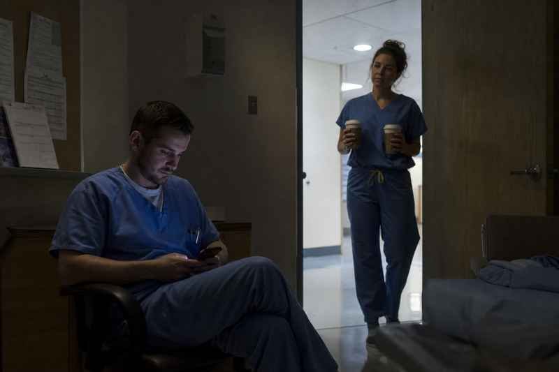 Surgical technologist in scrubs standing in a hospital corridor during a night shift, ready for an on-call case