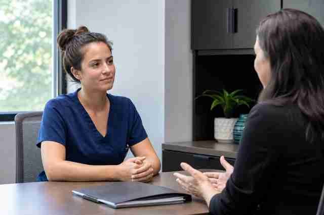Surgical technologist in scrubs discussing a job offer with a recruiter in an office
