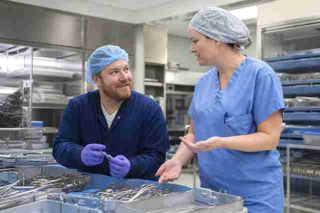 Sterile processing technician and a surgical technologist talking beside instrument trays
